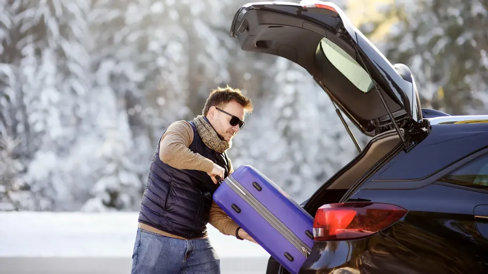 man packing luggage in car road trip